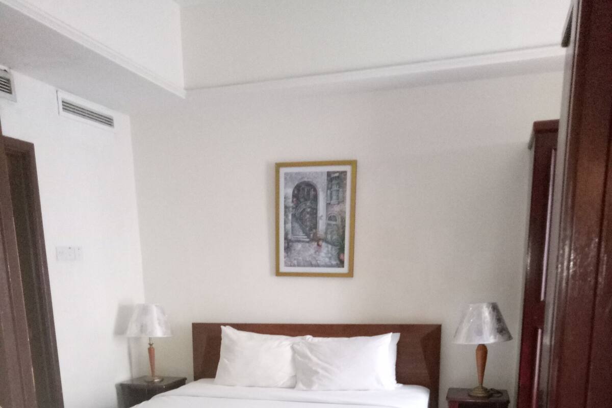 A hotel room with a bed, two bedside tables with lamps, a framed picture on the wall, and a carpeted floor.