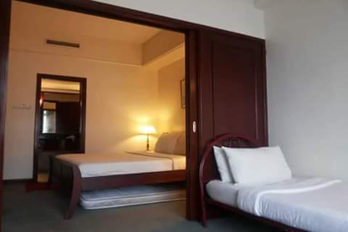 A hotel room with a bed, a bedside table, a lamp, and a door leading to another room.