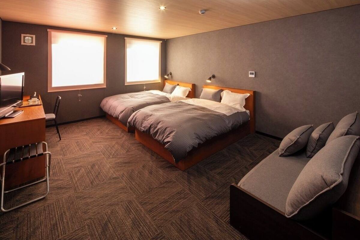 A hotel room with two beds, a desk with a chair, and a small sofa.