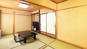 Ett traditionellt japanskt rum med tatamimattor på golvet, ett lågt bord, en tv och skjutdörrar.