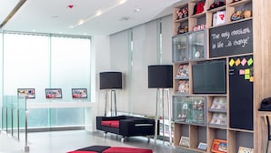 A modern waiting area with a red sofa, black and red cushions, a glass railing, and a wall with shelves displaying various items and a motivational quote.