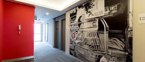 Un pasillo con una pared roja, un mural de un coche de carreras y un cartel con los números de las habitaciones.
