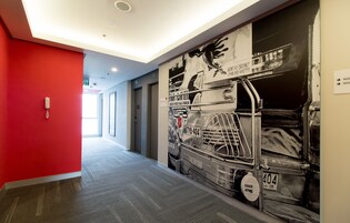 Un pasillo con una pared roja, un mural de un coche de carreras y un cartel con los números de las habitaciones.