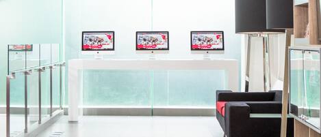 A modern reception area with three monitors on a white table, a black sofa, and a glass railing.