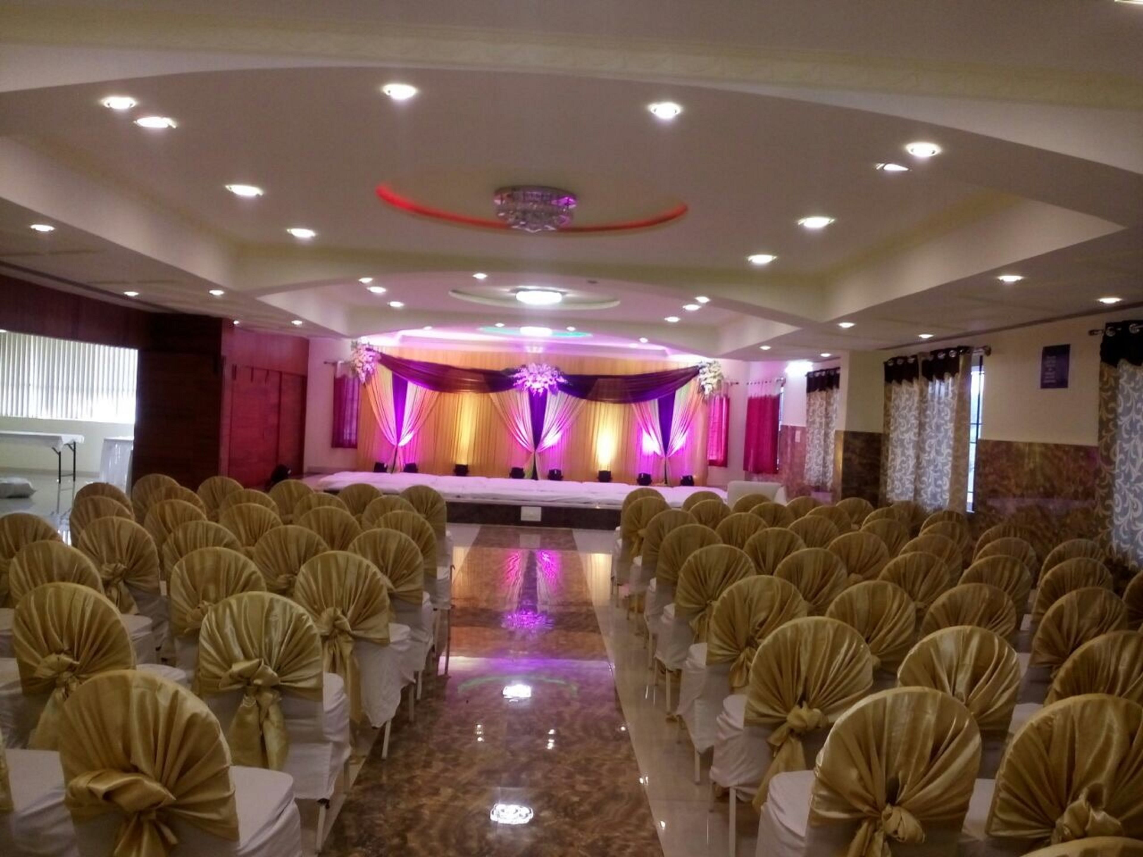 A banquet hall with rows of chairs, a stage with draped curtains, and a ceiling with recessed lighting.