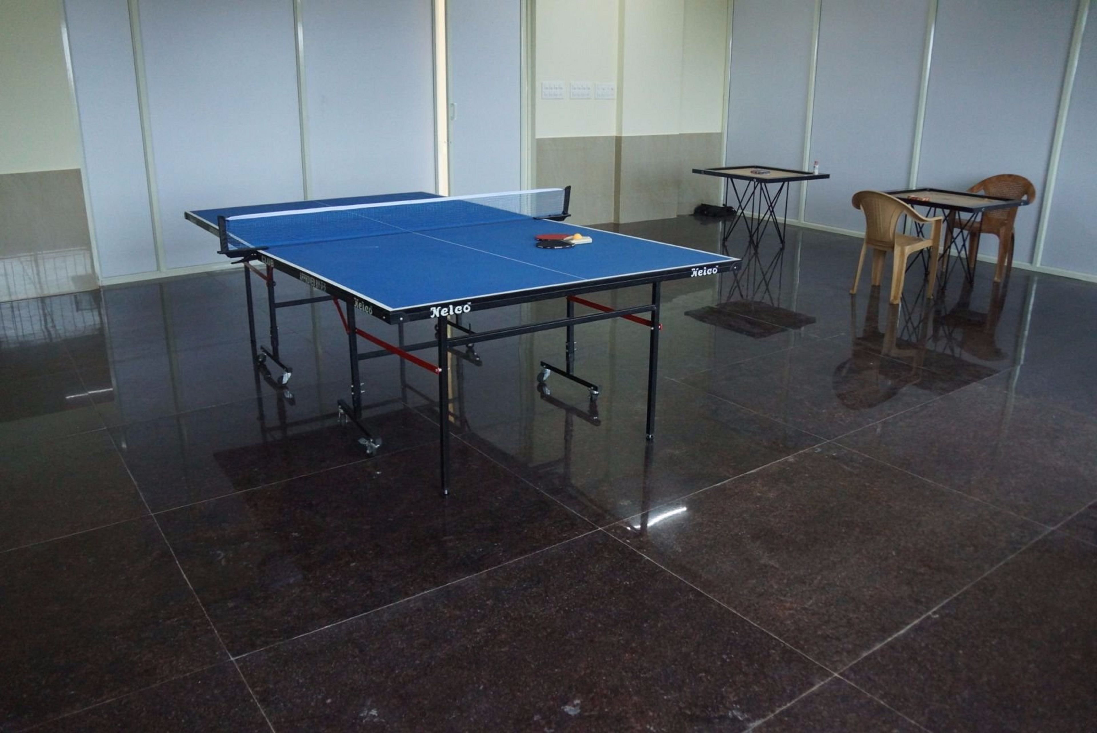 Una mesa de ping pong en una habitación con suelo de baldosas y dos pequeñas mesas con sillas.