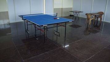 Una mesa de ping pong en una habitación con suelo de baldosas y dos pequeñas mesas con sillas.
