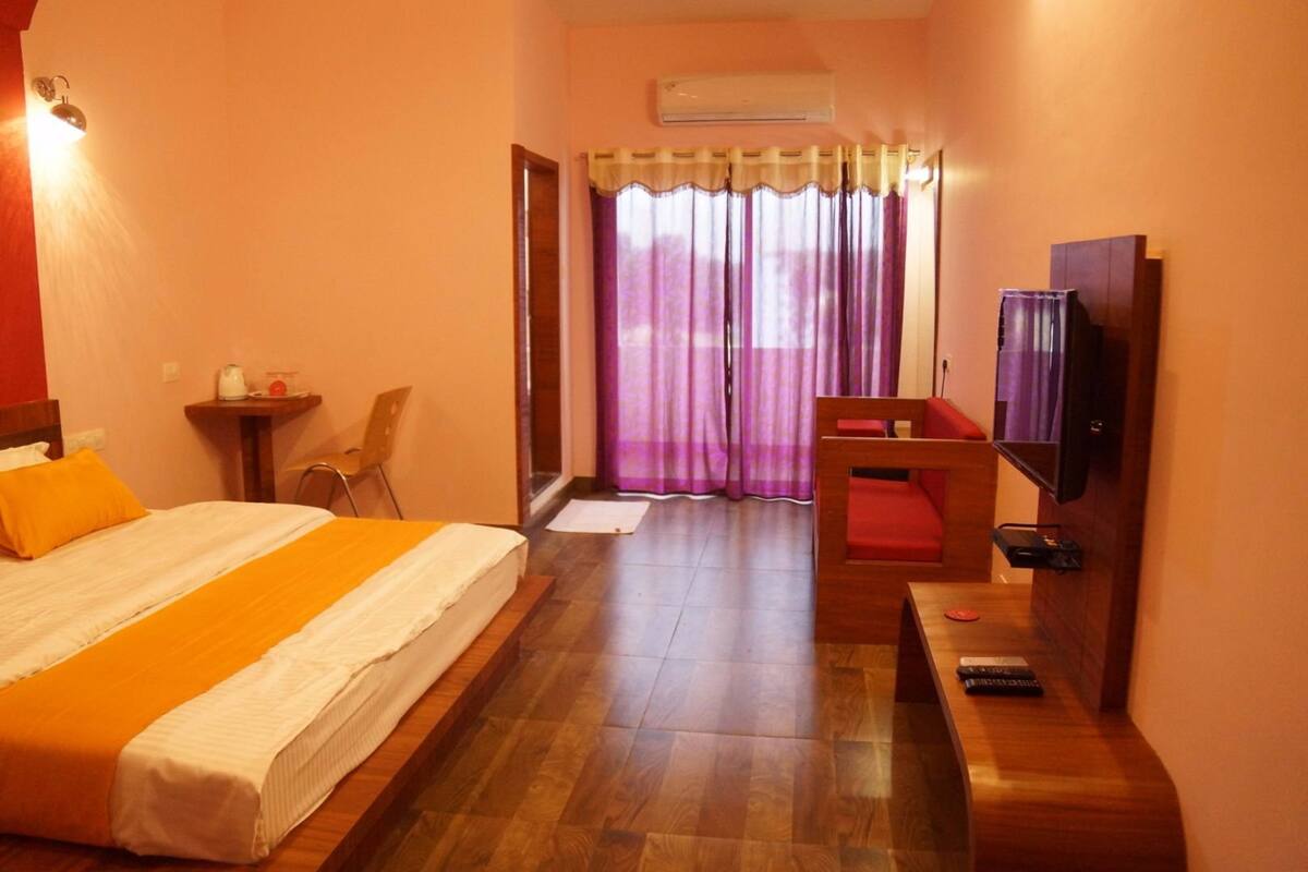 A hotel room with a large bed, a desk, a chair, a television, and a window with curtains.