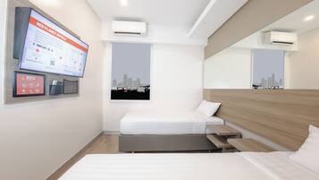 Una habitación de hotel con cama, escritorio, televisor montado en la pared y dos aires acondicionados.