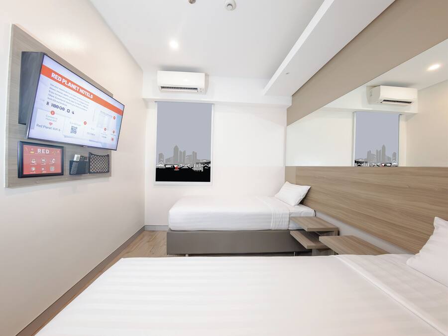 Una habitació d'hotel amb llit, escriptori, televisió penjada a la paret i dues unitats de aire condicionat.