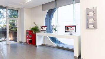 Un área de recepción con dos monitores de ordenador, una planta y una pared de vidrio.
