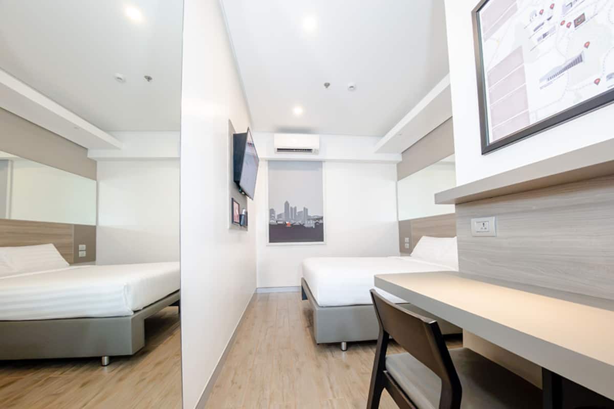 A modern hotel room with two beds, a desk, a chair, and a cityscape poster.