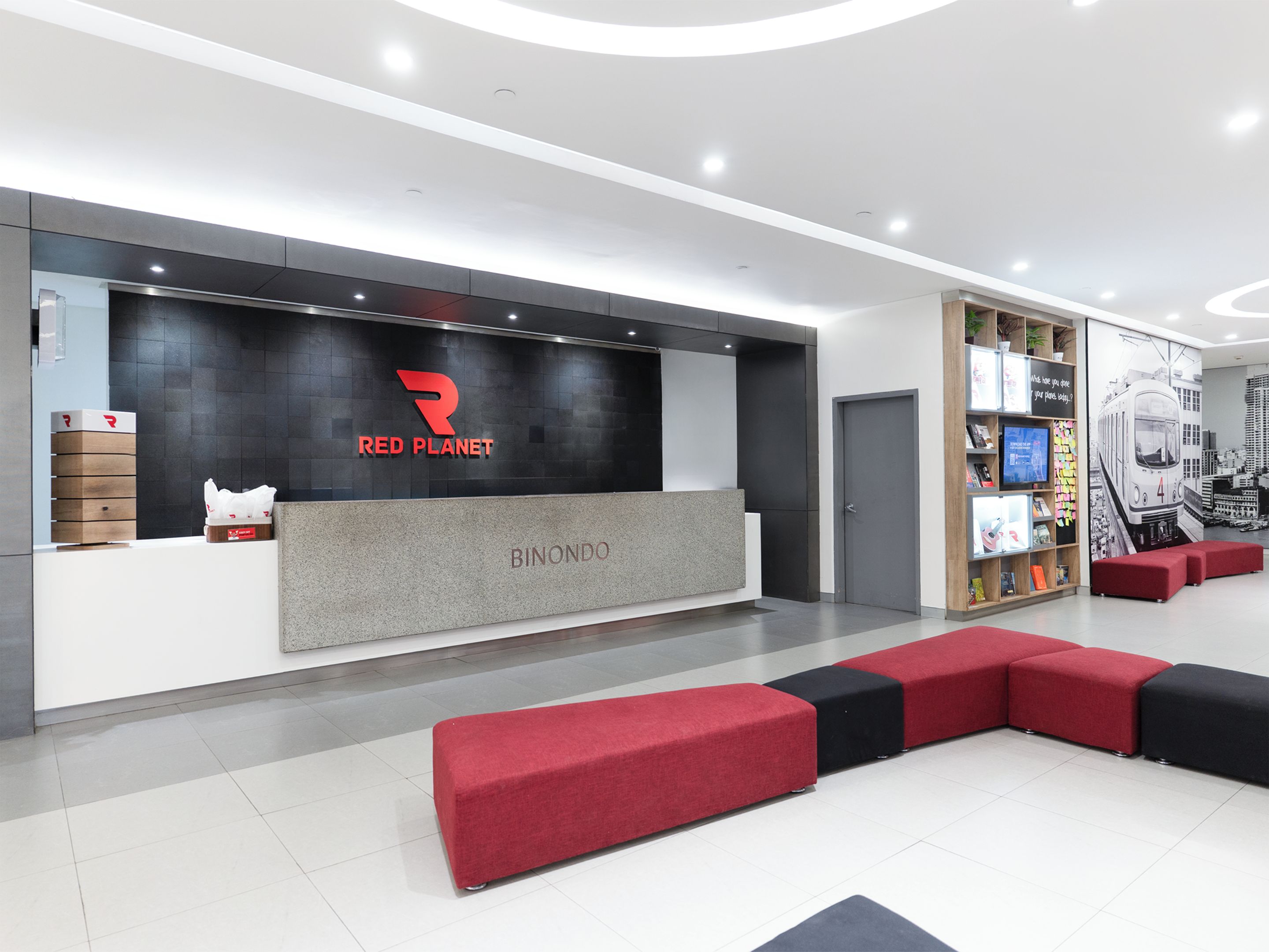 A modern reception area with a Red Planet logo, a counter, and a seating area with red and black cushions.