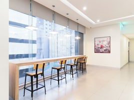 A modern bar area with a long counter and four bar stools, large windows with a city view, and a framed picture on the wall.