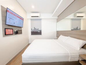 Una camera d'albergo moderna con un letto, una TV a muro che mostra informazioni dell'hotel, condizionatori e vista sulla città.
