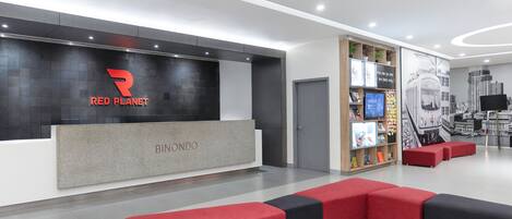Uma área de recepção moderna com o logotipo Red Planet, uma placa BINONDO e uma estante com diversos objetos.