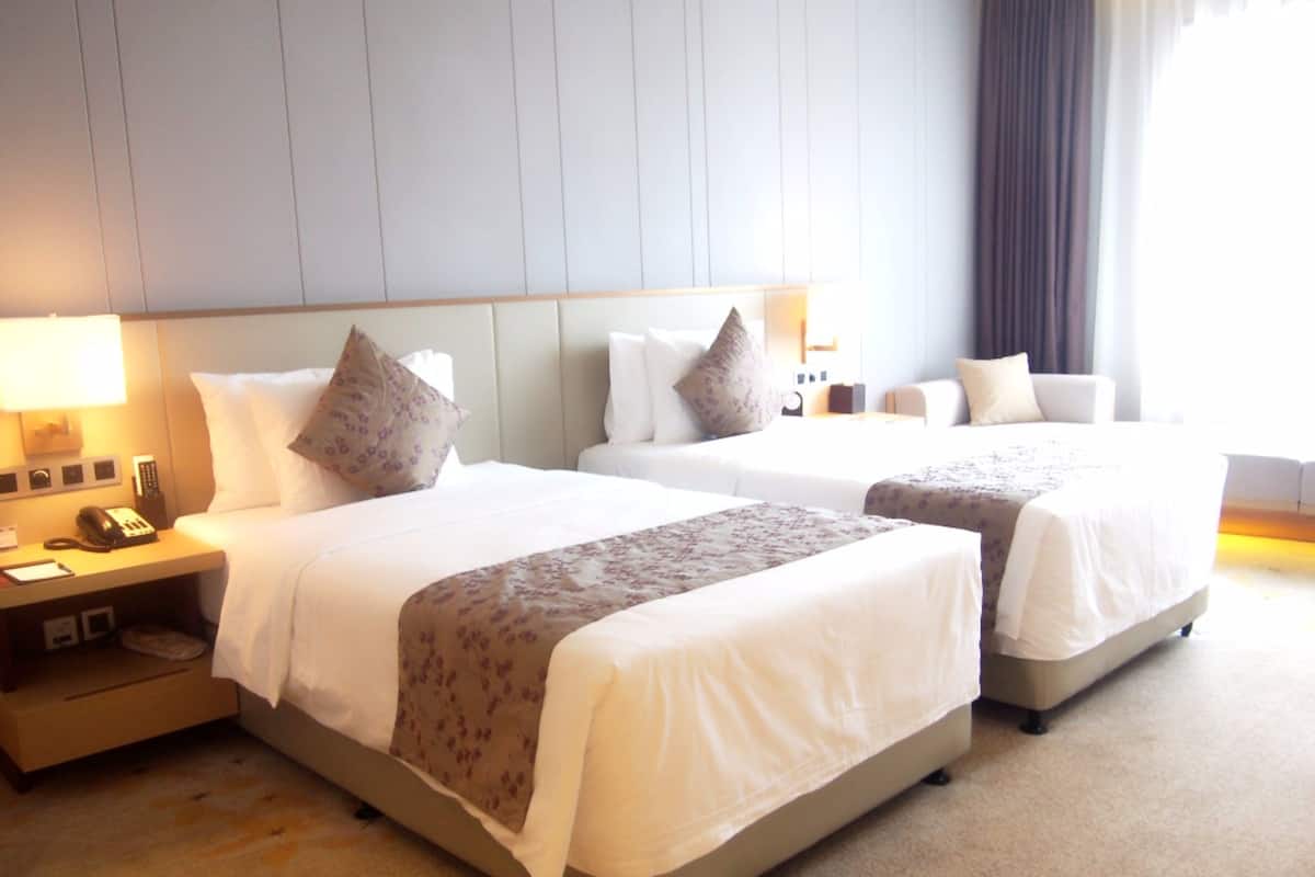 Una habitación de hotel con dos camas, una mesita de noche con lámpara y otro pequeño mueble con un teléfono.