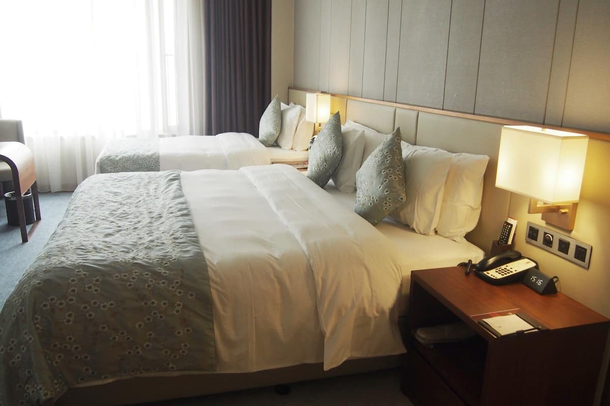 Una habitación de hotel con dos camas, un escritorio con teléfono y una mesita de noche con lámpara.
