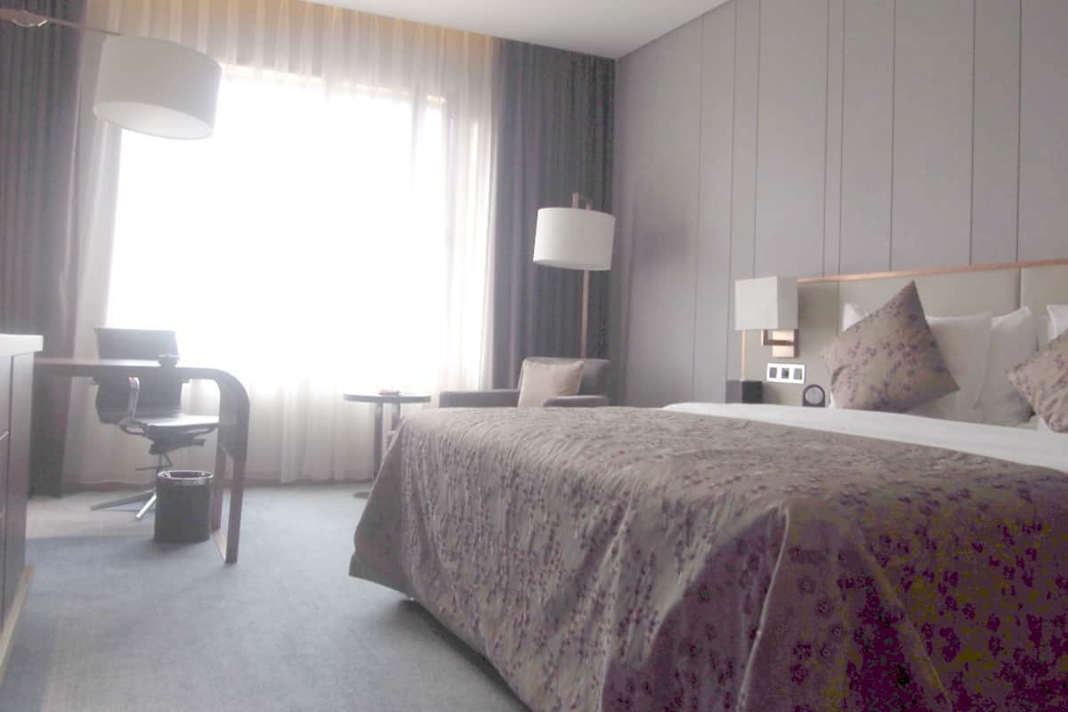 Una habitación de hotel con una cama grande, un escritorio con una silla, una mesita y una lámpara.