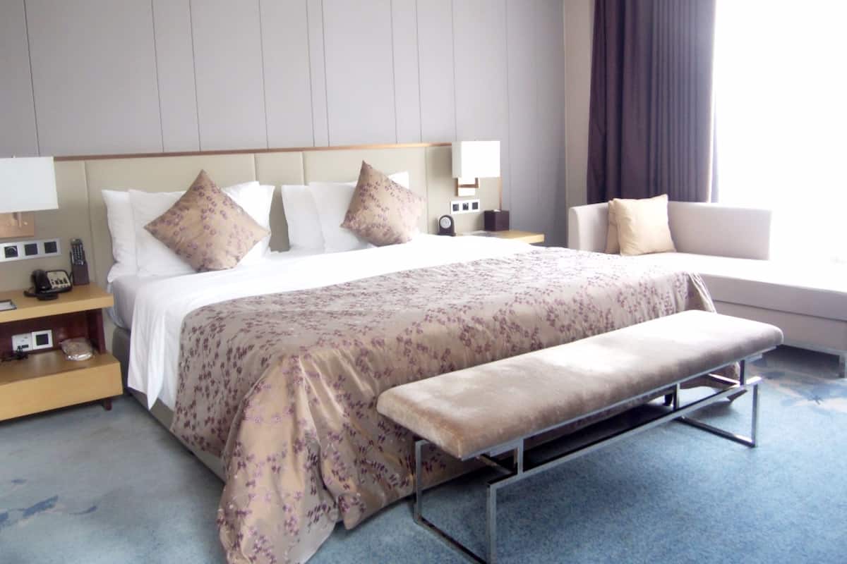Una habitación de hotel con una cama grande, una mesita de noche con lámpara, un reloj despertador y un sofá.