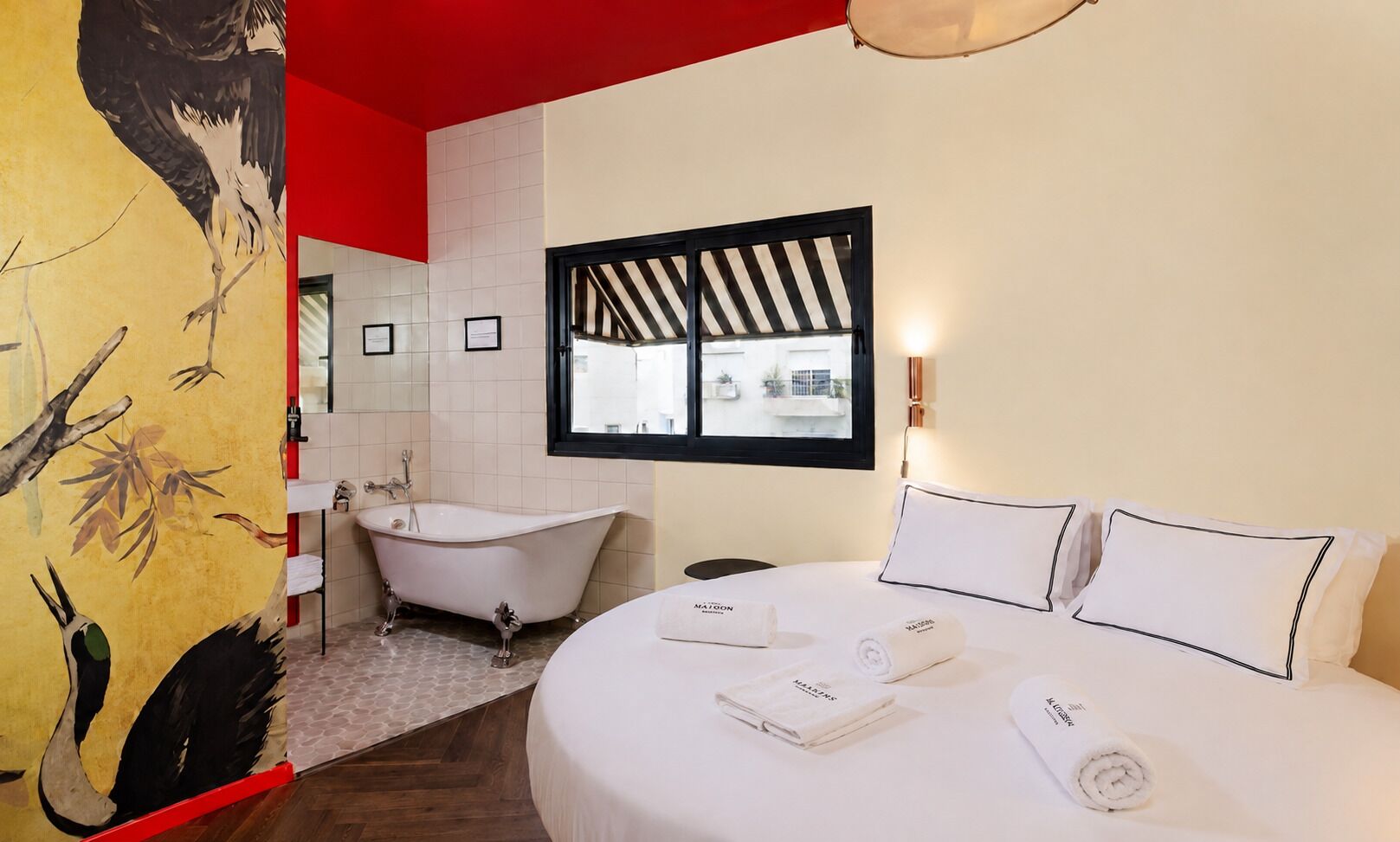 A hotel room with a large bed, a bathtub, and a window with a view of buildings.