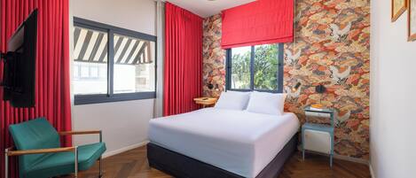 A bedroom with a bed, a chair, a nightstand, a TV, and a window with curtains.
