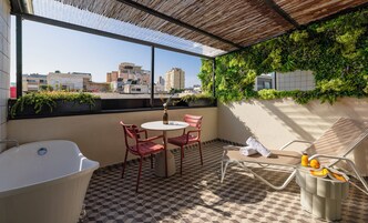 Una terraza en la azotea con suelo a cuadros, una bañera blanca, dos sillas rojas, una mesa blanca y una botella de vidrio.