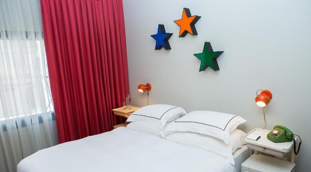 Una habitación de hotel con una cama, cortinas rojas y tres estrellas fijadas a la pared.