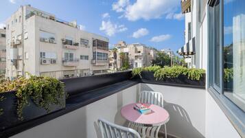 A balcony with a small table and chairs, potted plants, and a view of surrounding buildings.