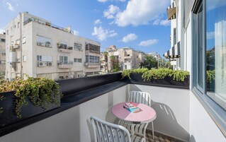 A balcony with a small table and chairs, potted plants, and a view of surrounding buildings.