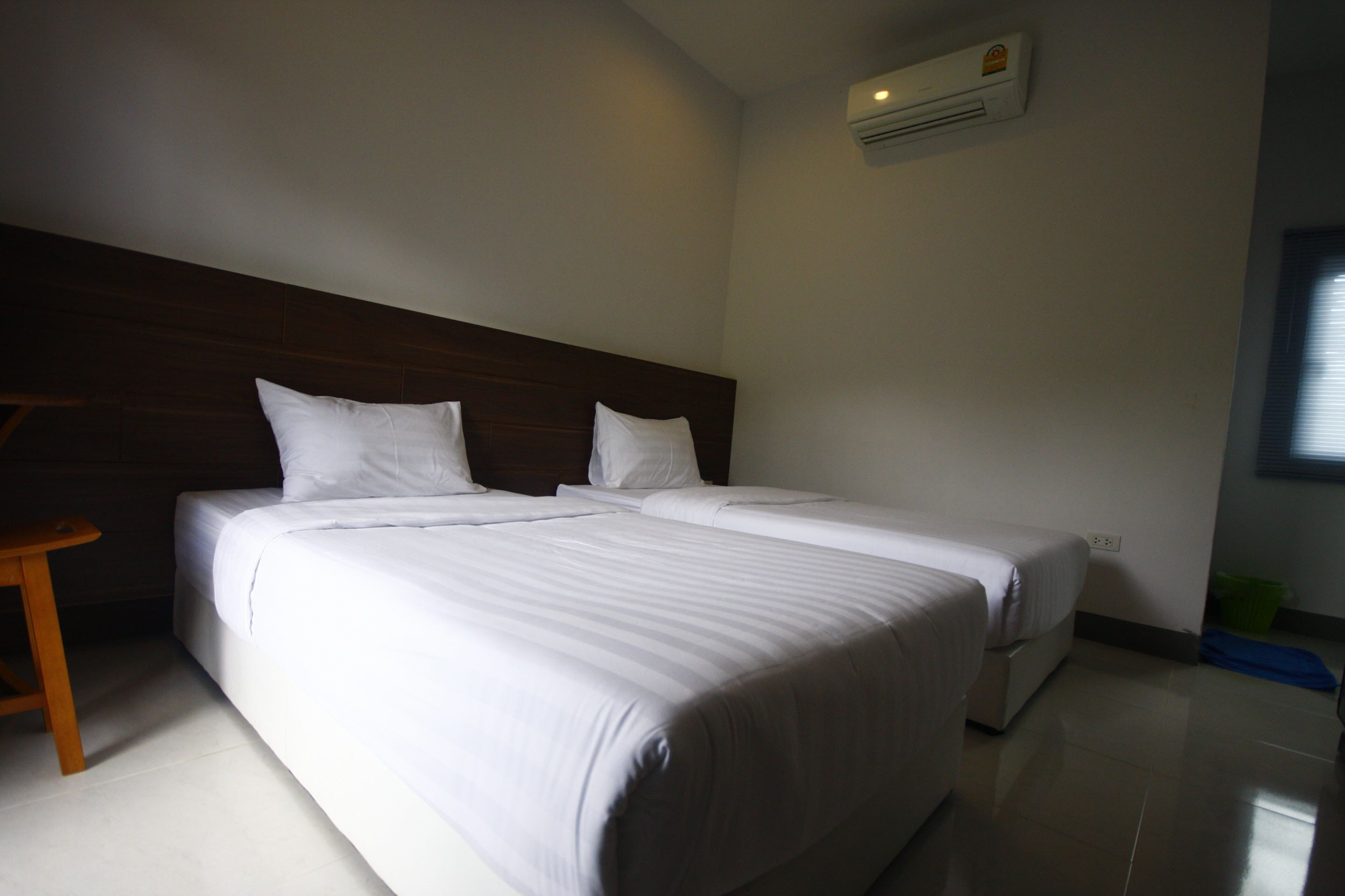 A hotel room with two beds, a wooden headboard, a small wooden stool, and a green trash bin.