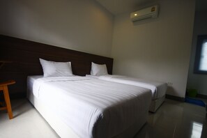 A hotel room with two beds, a wooden headboard, a small wooden stool, and a green trash bin. - Grand Garden Home Resort (Buriram)