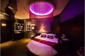 Une chambre d’hôtel moderne avec un grand lit, un luminaire rond au plafond et une petite table avec une lampe.
