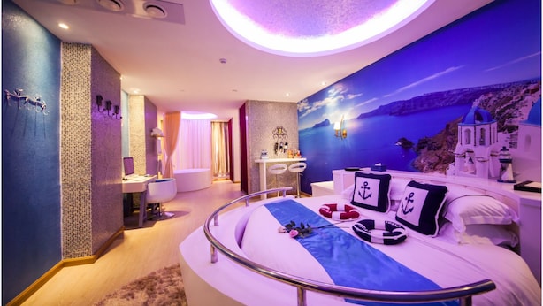 A modern hotel room with a curved bed, a view of the sea, and a sunset mural. - Brightman Theme Hotel (Foshan)