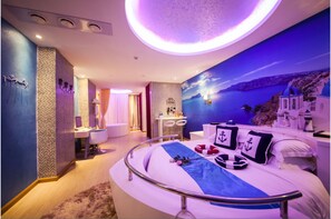 A modern hotel room with a curved bed, a view of the sea, and a sunset mural. - Brightman Theme Hotel (Foshan)