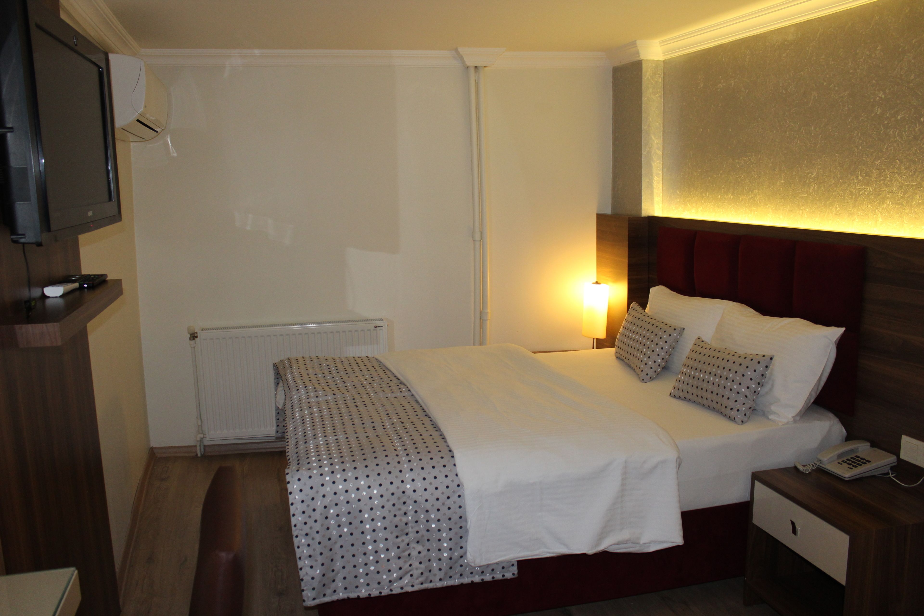 A hotel room with a bed, bedside table, lamp, and a television on a stand.