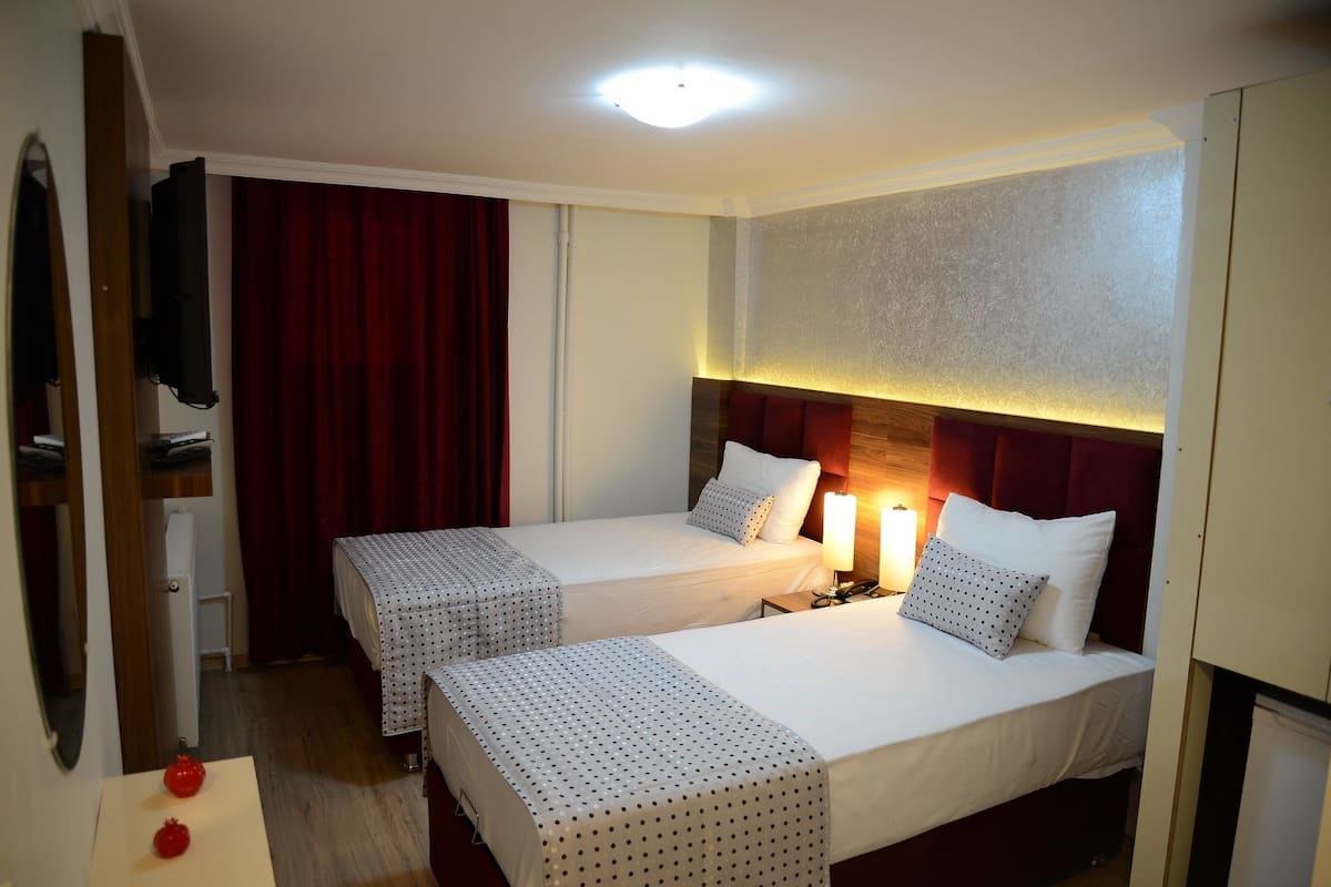 A hotel room with two beds, a TV, a desk, and a red curtain.