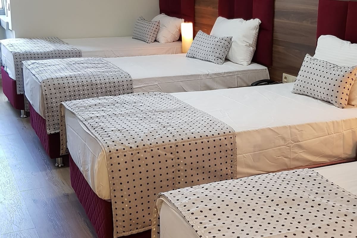 A hotel room with four beds arranged in a row, each with a red headboard and white bedding with a polka dot pattern.