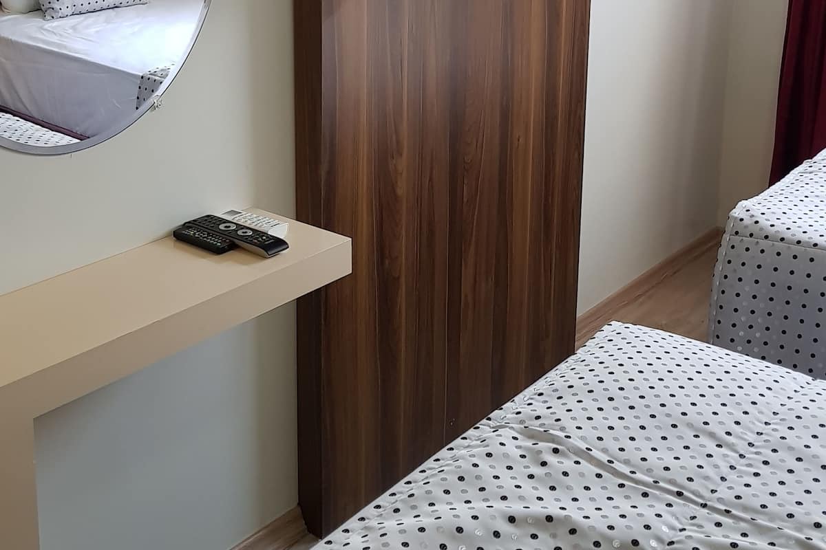A hotel room with a bed, a TV mounted on a wooden panel, a mirror, and a small table with a remote control.