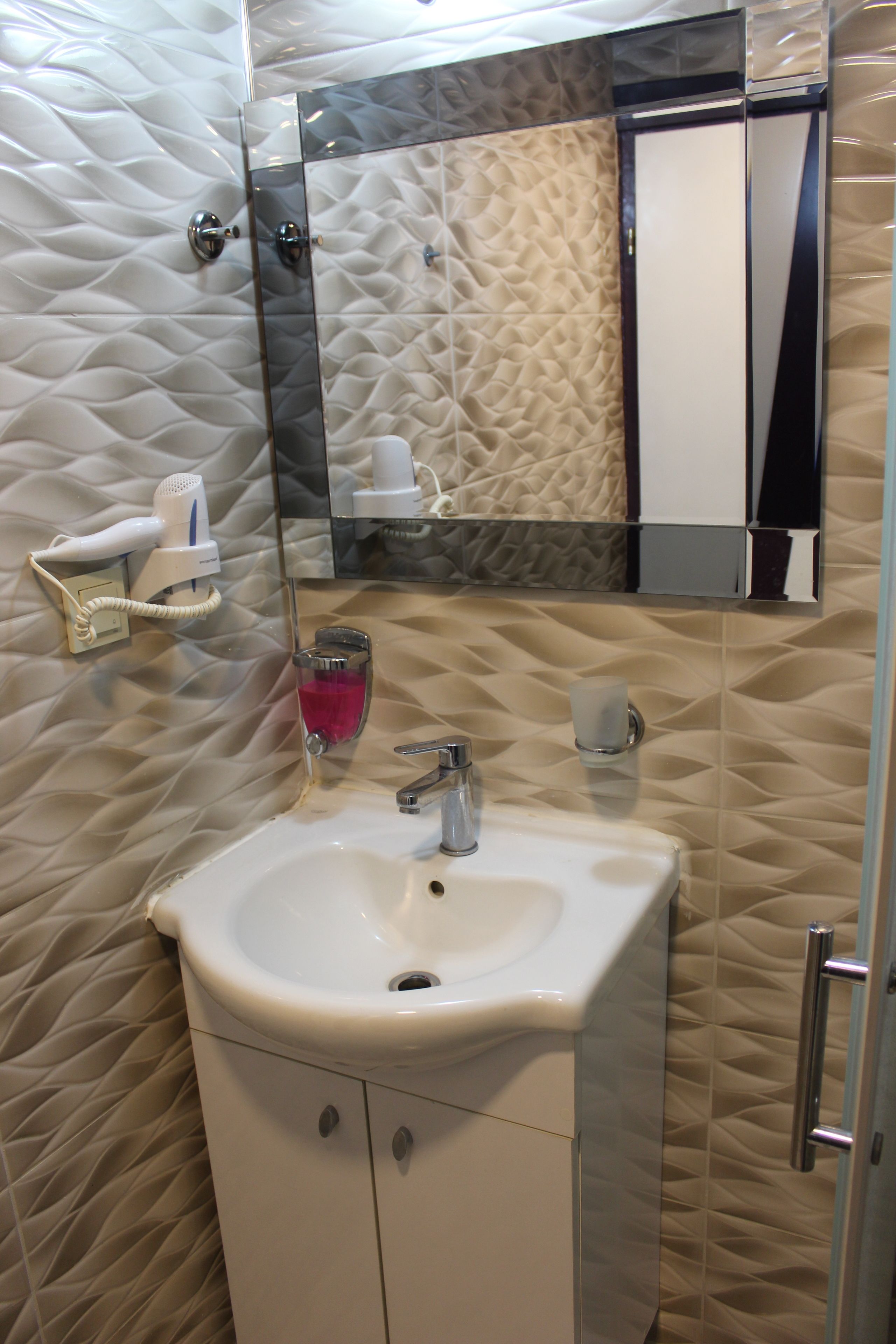 Une salle de bain avec un mur à texture, un lavabo blanc, un miroir et un sèche-cheveux.