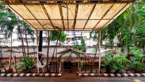A covered outdoor area with a central seating area, surrounded by potted plants and trees. - Hotel Balwas International (Mumbai)
