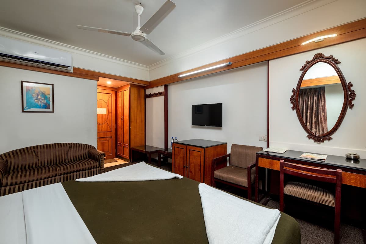 Quarto de hotel com cama, escrivaninha, cadeira, televisão e guarda-roupa.
