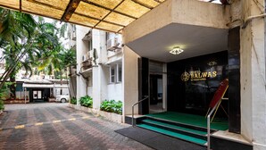 A hotel entrance with a green carpeted staircase, a covered outdoor area with a tiled floor, and a white car parked nearby. - Hotel Balwas International (Mumbai)