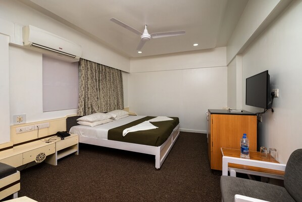 Una habitación de hotel con cama, escritorio, silla, televisor, armario y aire acondicionado.