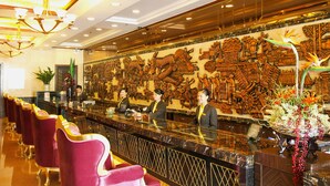 A hotel lobby with a reception desk, staff, and a decorative wall. - Golden City Hotel (Foshan)