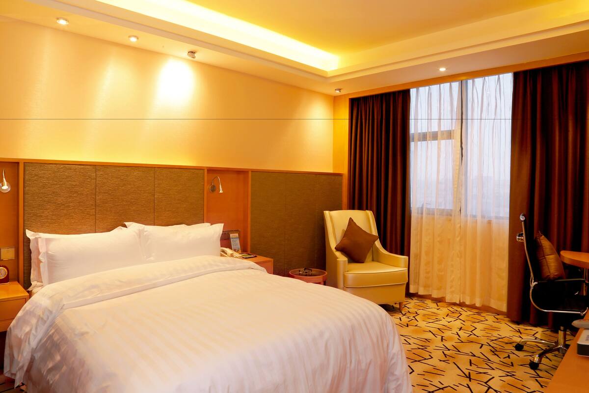 A hotel room with a large bed, a chair, a desk, and a window with curtains.