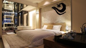 A modern hotel room with a large bed, a bedside table with a lamp, a mirror, and a decorative wall piece. - Golden City Hotel (Foshan)
