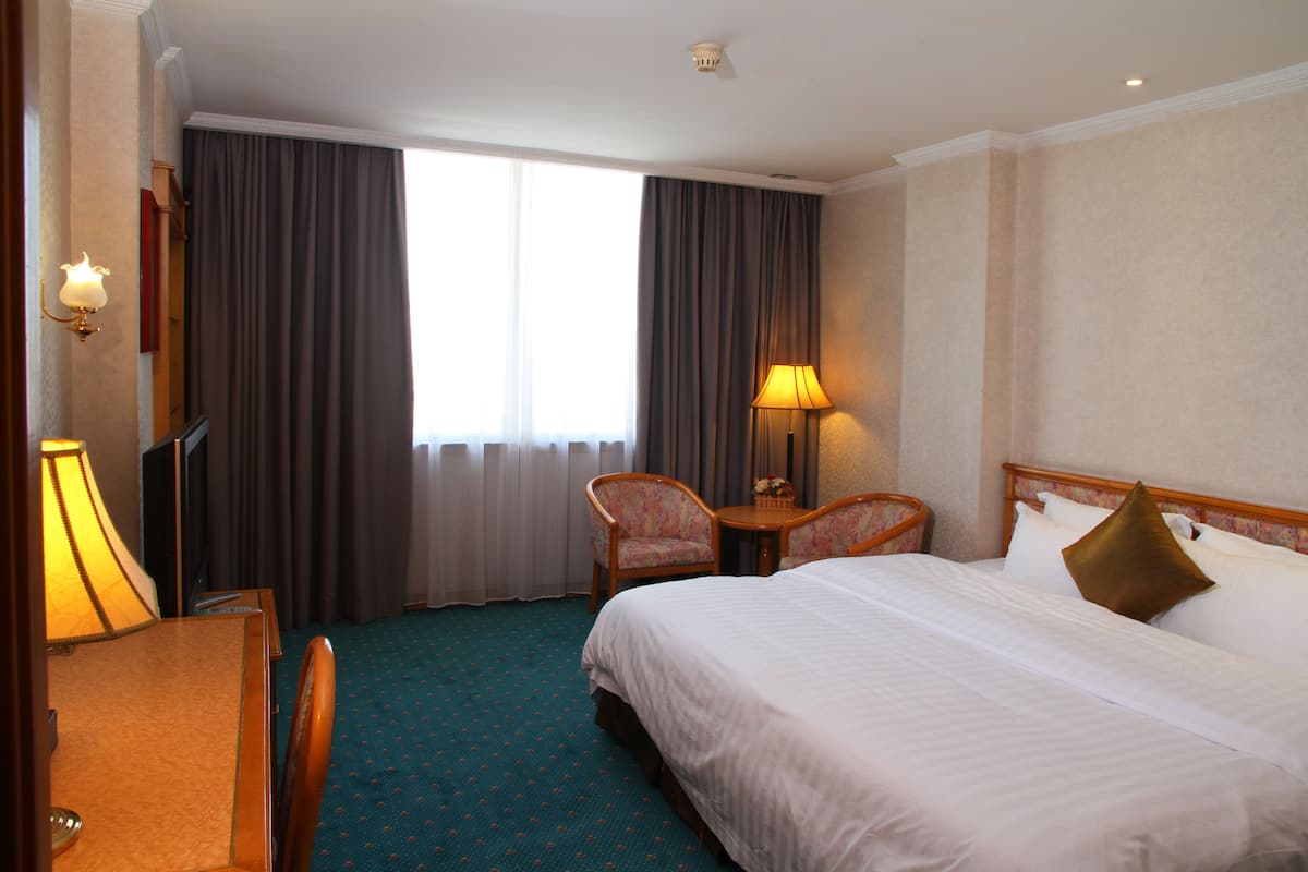 A hotel room with a large bed, two chairs, a desk, and a lamp.
