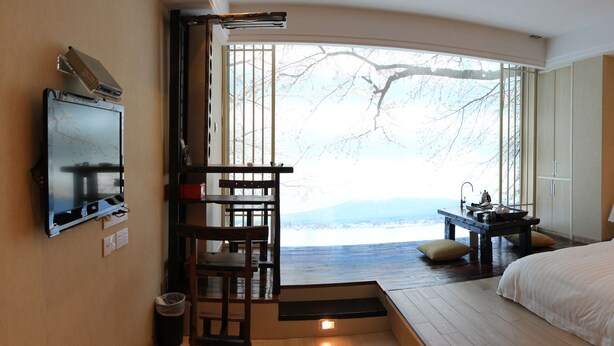 A hotel room with a bed, a desk, a chair, a TV, and a view of the outdoors. - Golden City Hotel (Foshan)