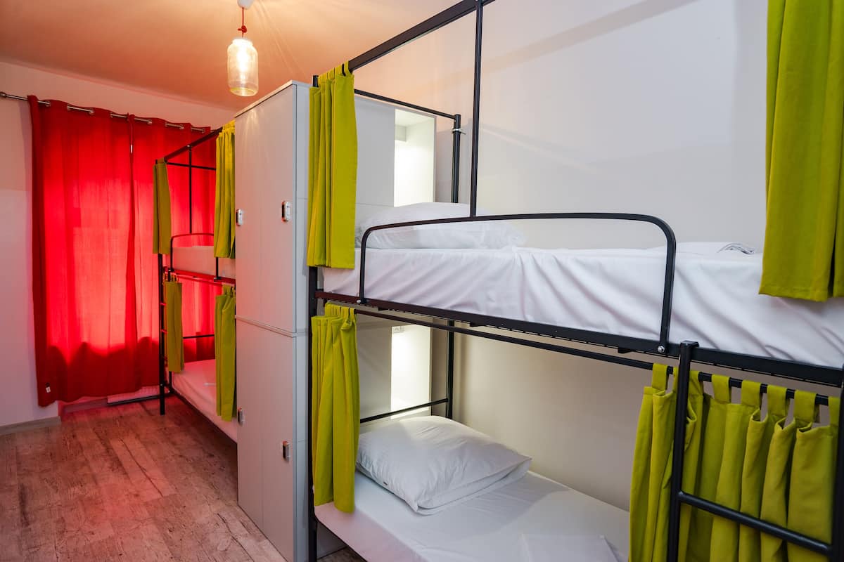A dormitory room with bunk beds, red curtains, and a hanging light fixture.